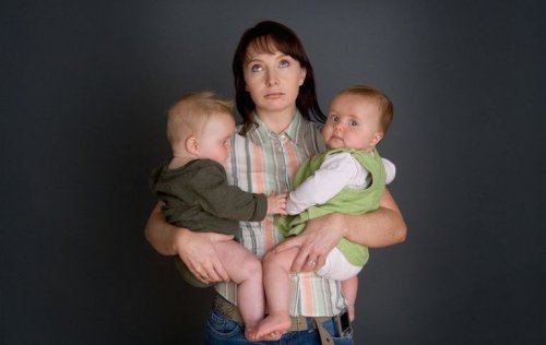 udmattet mor med to børn i armene