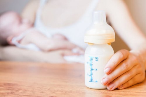 Mor holder babyflaske mens hun ammer baby