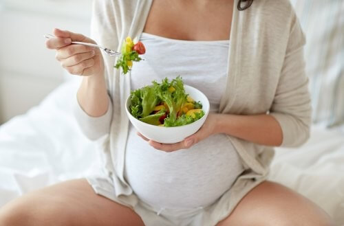 Gravid kvinde spiser en skål salat