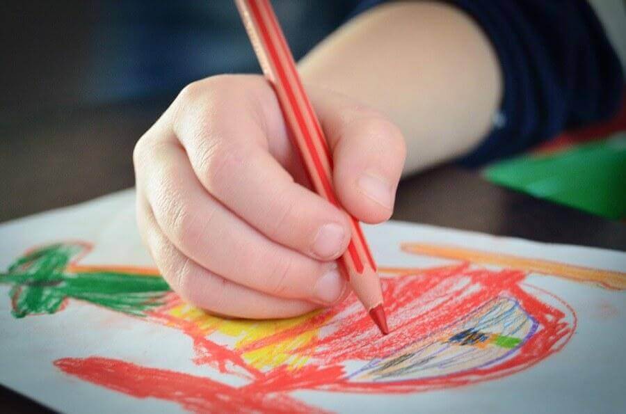 Barn tegner med rød farveblyant på farverig tegning.