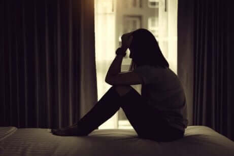 Tips til forebyggelse af depression efter adoption: Kvinde sidder fortvivlet på en seng i et mørkt soveværelse.