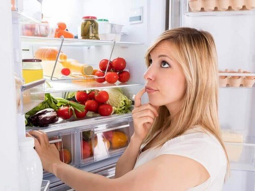 Kvinde står og tænker ved køleskabet 