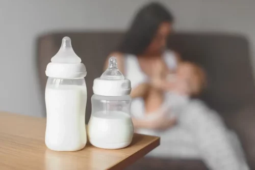 Mor ammer, mens der står flasker på bordet, som repræsenterer modermælkserstatning i babyers kost