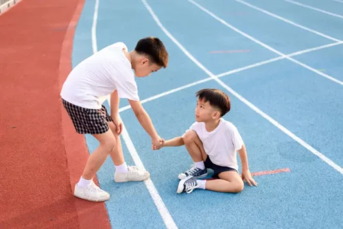 To børn på en løbebane hjælper hinanden