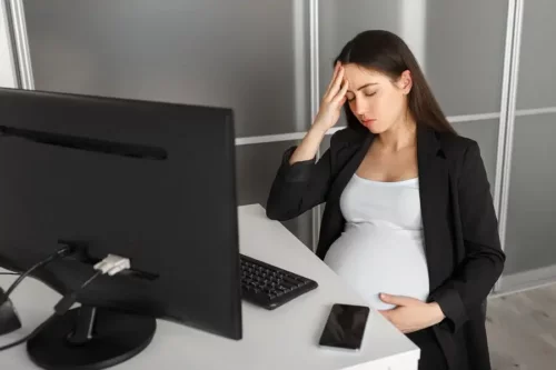 Træt gravid kvinde på kontor tager sig til hovedet