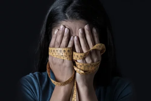 Kvinde med målebånd om hænderne skjuler sit ansigt og repræsenterer spiseforstyrrelser i den perinatale fase