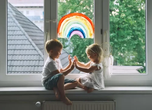 To børn sidder foran vindue med regnbue