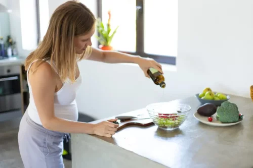 Kvinde laver salat for at indtage olivenolie under graviditet
