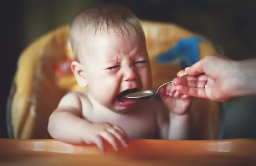 Baby, der tilbydes mad, græder, hvilket repræsenterer anoreksi hos småbørn