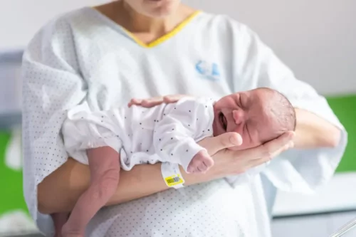 Kvinde står med nyfødt baby på armen
