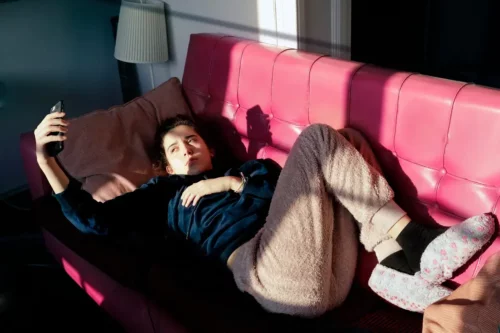 Teenager ligger med telefon på sofa og repræsenterer social isolation hos unge