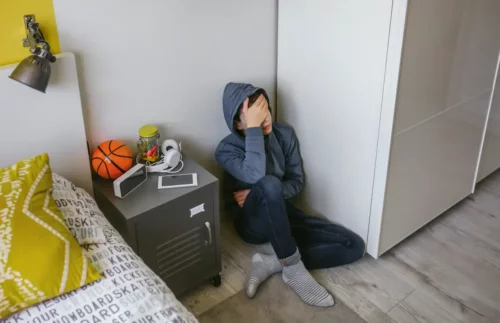 Trist dreng sidder på gulv som følge af psykologisk vold