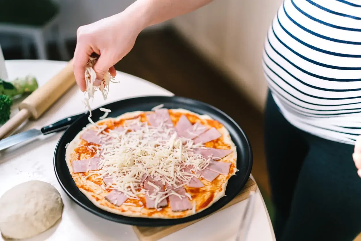 Gravid kvinde laver pizza, da man godt må spise skinke under graviditet