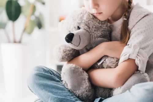 En pige krammer en bamse og oplever ensomhed i barndommen