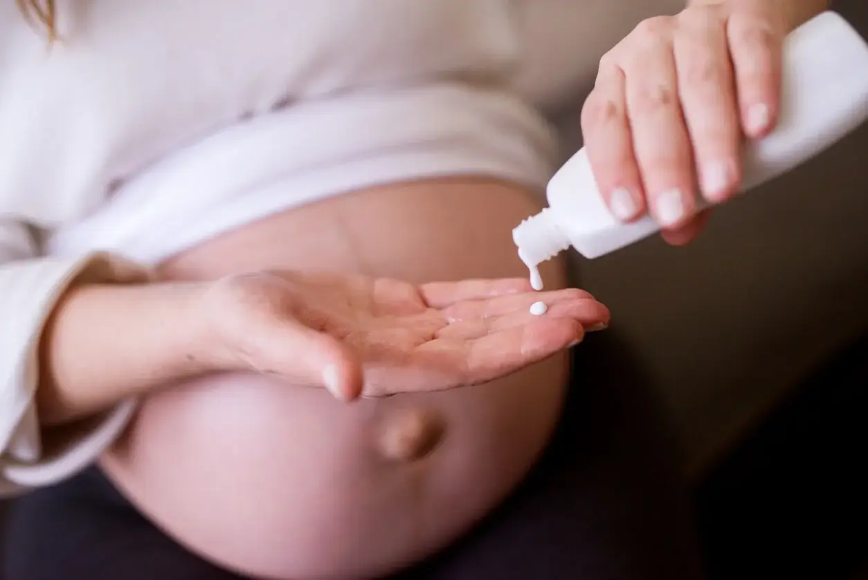 Gravid kvinde står med creme og viser behovet for at undgå de forbudte hudplejeingredienser under graviditet
