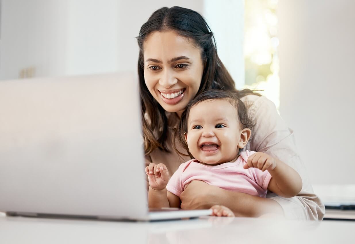 Mor sidder med baby ved computer